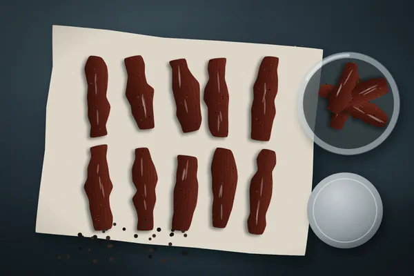 Strips of homemade smoked beef jerky on parchment with a glass jar and peppercorns